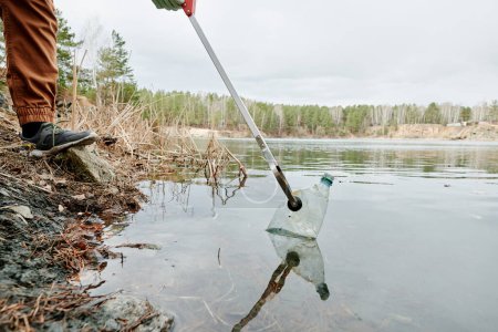 Foto de Imagen recortada del hombre recogiendo botellas de plástico sucio del lago - Imagen libre de derechos