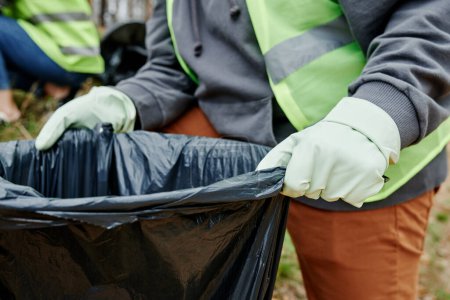 Téléchargez les photos : Image rapprochée d'un bénévole tenant un gros sac poubelle pour les ordures collectées dans un parc municipal - en image libre de droit