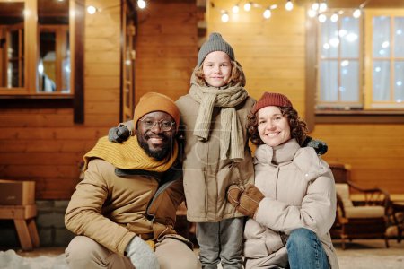 Téléchargez les photos : Joyeux père et mère interculturels dans des vêtements d'hiver chauds entourant leur petit fils mignon heureux tout en profitant des vacances d'hiver - en image libre de droit