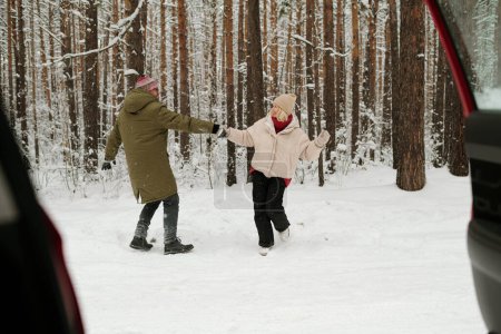 Photo for Happy senior couple in winterwear having fun and dancing in pinetree forest while enjoying weekend in front of their car with open door - Royalty Free Image