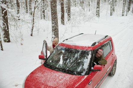 Téléchargez les photos : Heureux voyageurs matures regardant hors de leur voiture tout en profitant d'une belle vue sur la forêt d'hiver couverte de neige pendant le week-end voyage - en image libre de droit