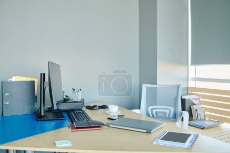 Foto de Lugar de trabajo del director de oficina o diseñador con dispositivos móviles y otros suministros en el escritorio de pie junto a la pared gris y ventana grande - Imagen libre de derechos