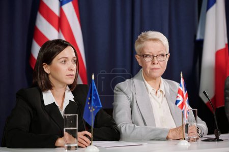 Photo for Mature and young female delegates representing European Union and Great Britain listening to foreign colleague at summit or conference - Royalty Free Image