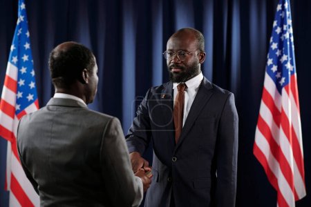 Photo for New president of USA keeping right hand on Holy Bible during oath of office while standing in front of mature African American man - Royalty Free Image