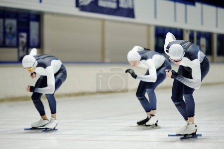 Téléchargez les photos : Groupe de jeunes sportifs en uniforme sportif glissant le long de la patinoire dans une grande arène moderne prenant part à une course de patinage de vitesse sur piste courte - en image libre de droit