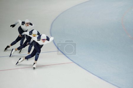 Drei junge aktive Sportler gleiten auf Schlittschuhen über die Eisbahn, während sie vor dem Wettkampf einige Übungen üben
