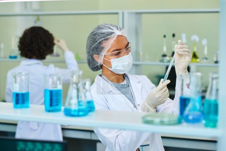 Foto de Virologista o farmacóloga joven sosteniendo frasco con sustancia química líquida azul durante un experimento científico en laboratorio - Imagen libre de derechos