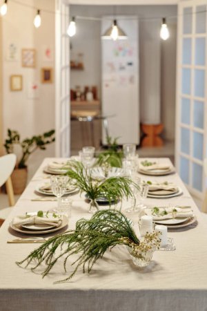 Téléchargez les photos : Longue table servie pour le dîner de famille ou la célébration de l'événement de la vie avec des bougies, des plantes vertes, des assiettes, des flûtes pour boissons et autres choses - en image libre de droit