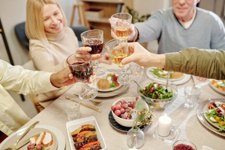 Téléchargez les photos : Haut angle des mains des membres de la famille interculturelle griller avec des verres de vin fait maison sur la table servi avec de la nourriture appétissante - en image libre de droit