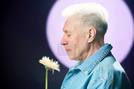 Téléchargez les photos : Vue latérale de l'homme âgé regardant la fleur fleurir la nuit et sentant son odeur tout en se tenant contre la pleine lune et le ciel sombre - en image libre de droit