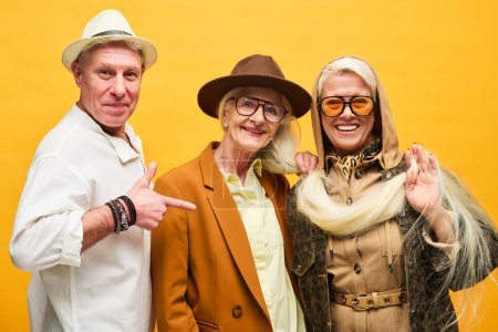 Photo for Group of happy and stylish senior people in dopamine dressing looking at camera while posing against yellow background in studio - Royalty Free Image