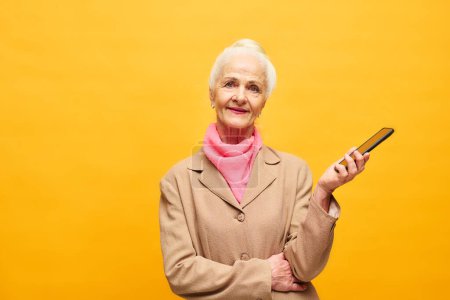 Foto de Elegante mujer mayor con teléfono inteligente en la mano de pie delante de la cámara en aislamiento y posando durante la sesión de fotos - Imagen libre de derechos