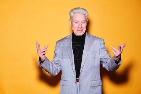 Photo for Senior businessman in formalwear keeping arms bend in elbows and stretching some fingers while standing against yellow background - Royalty Free Image