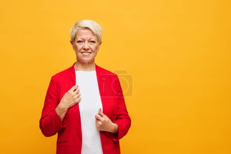 Téléchargez les photos : Blonde jolie femme en tenue décontractée intelligente regardant la caméra tout en se tenant en isolement sur fond jaune avec copyspace sur sa gauche - en image libre de droit
