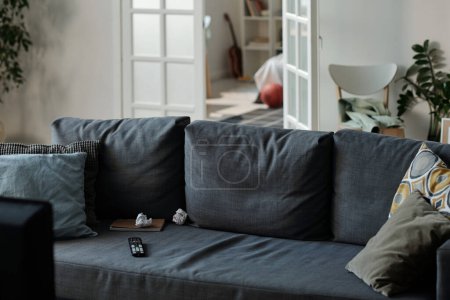 Téléchargez les photos : Canapé confortable gris avec plusieurs oreillers doux debout dans le centre du salon contre la porte ouverte et une partie de la chambre confortable - en image libre de droit