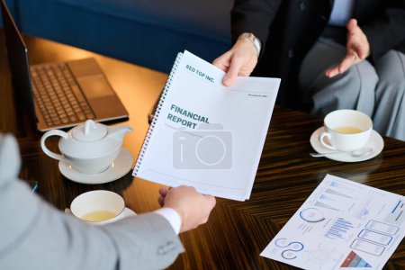 Photo for Close-up of female hand passing financial report to colleague or business partner over table with two cups, teapot and document with charts - Royalty Free Image