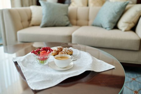 Téléchargez les photos : Petit déjeuner composé d'une tasse de café, de baies rouges et de pâtisserie sur une serviette en coton blanc propre debout sur une petite table ronde dans la chambre d'hôtel - en image libre de droit