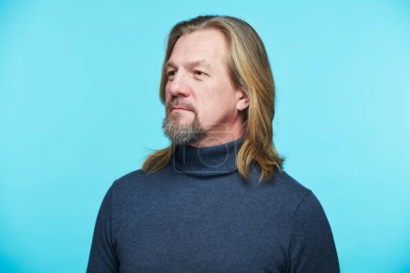 Téléchargez les photos : Portrait d'homme barbu mature aux cheveux longs regardant loin debout sur fond bleu - en image libre de droit