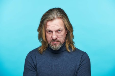 Photo for Mature man with displeased expression looking at camera standing against blue background - Royalty Free Image