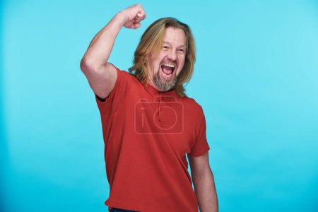 Photo for Portrait of happy mature man raising his arm satisfying with something isolated on blue background - Royalty Free Image