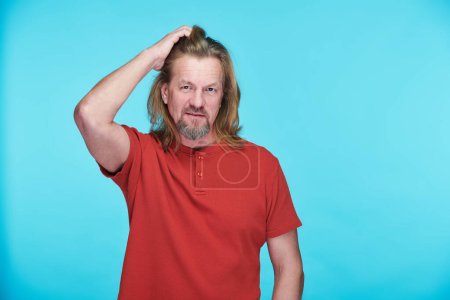 Photo for Portrait of handsome mature man with long hair looking at camera standing on blue background - Royalty Free Image