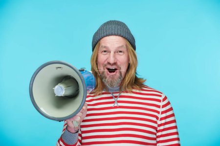 Photo for Portrait of mature man looking at camera and using speaker to announce advert standing on blue background - Royalty Free Image
