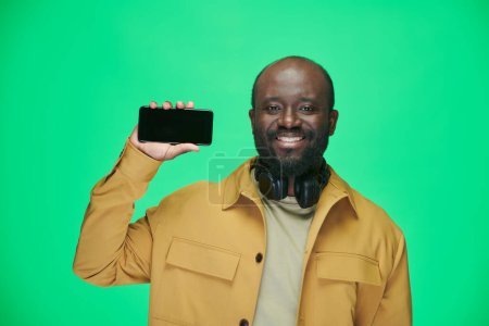 Foto de Retrato del hombre afroamericano sonriendo a la cámara mostrando la aplicación en su teléfono móvil de pie sobre el fondo verde - Imagen libre de derechos
