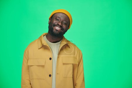Téléchargez les photos : Portrait de l'homme afro-américain dans des vêtements élégants souriant à la caméra debout sur fond vert - en image libre de droit