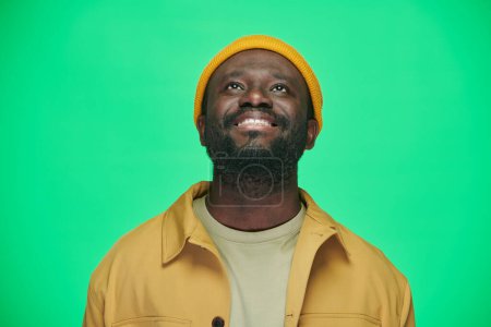 Photo for Portrait of African American smiling man in hat looking up standing on green background - Royalty Free Image