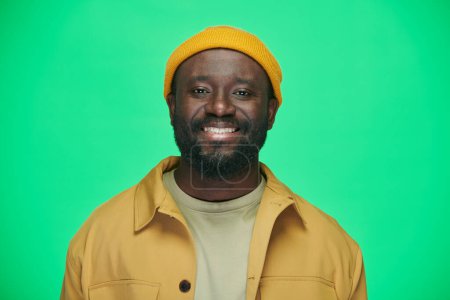 Photo for Portrait of smiling African American man in yellow hat looking at camera standing on green background - Royalty Free Image