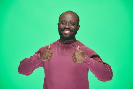 Photo for Portrait of happy African American man showing thumbs up and smiling at camera standing on green background - Royalty Free Image