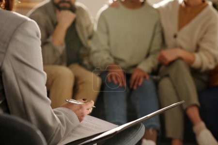 Photo for Close-up of social worker making notes in document while talking to foster parents at meeting at home - Royalty Free Image