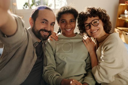 Portrait of happy family with adopted daughter smiling at camera while making selfie portrait