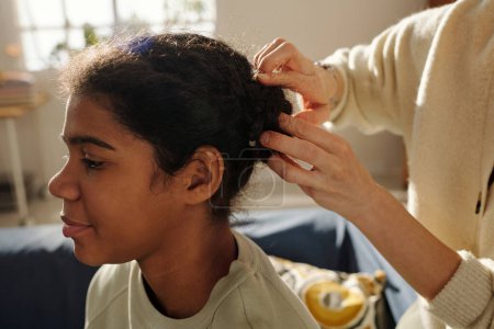 Téléchargez les photos : Gros plan de la mère faisant coiffure à sa fille adoptive afro-américaine la préparant à l'école - en image libre de droit