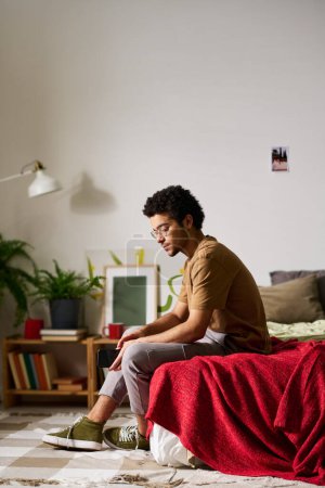 Photo for Vertical image of sad teenage boy sitting on bed in his bedroom and thinking about something - Royalty Free Image