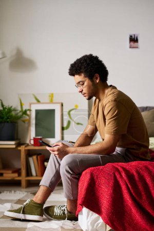 Foto de Imagen vertical del triste adolescente leyendo el mensaje en el teléfono inteligente mientras está sentado solo en la cama en su dormitorio - Imagen libre de derechos