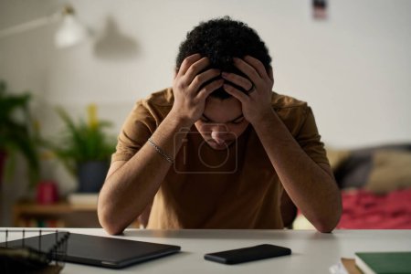 Téléchargez les photos : Jeune homme dans la dépression tenant les têtes assises au bureau et inquiet de ses problèmes - en image libre de droit