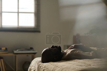 Téléchargez les photos : Afro-Américain dans la mélancolie couché sur le lit seul dans sa chambre - en image libre de droit