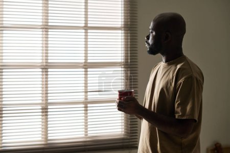 Téléchargez les photos : Pensive homme afro-américain regardant la fenêtre tout en buvant du café le matin - en image libre de droit