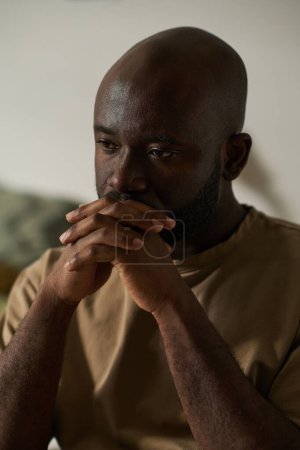 Photo for Vertical image of African American man thinking about something sitting alone in his room - Royalty Free Image