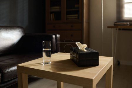 Téléchargez les photos : Petite table carrée en bois avec verre d'eau pure et boîte noire contenant des tissus préparés pour les patients de psychothérapeute - en image libre de droit