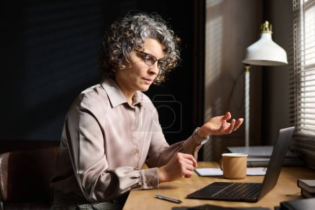 Foto de Psicoterapeuta maduro de confianza hablando con el paciente durante la cita o sesión en línea mientras está sentado frente a la computadora portátil en la oficina - Imagen libre de derechos