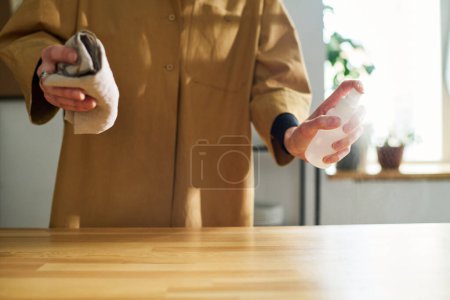 Téléchargez les photos : Gros plan de la jeune employée du café avec désinfectant pulvérisateur sur le comptoir pendant le nettoyage au début de la journée de travail - en image libre de droit