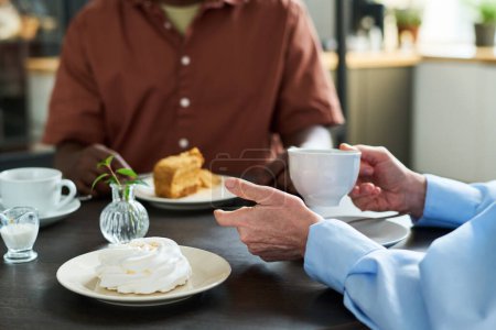 Foto de Primer plano de la mujer madura sosteniendo la taza de café durante el almuerzo con su marido mientras ambos sentados junto a la mesa servida en la cafetería y hablando - Imagen libre de derechos