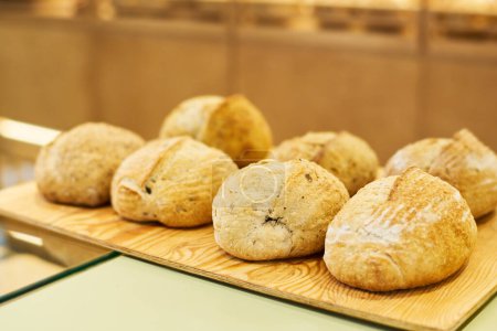 Foto de Varios panes de pan de trigo fresco sobre tabla de madera o bandeja en exhibición o mostrador preparado para vender a los clientes de la panadería - Imagen libre de derechos