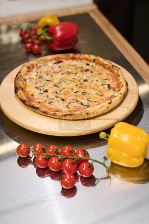 Téléchargez les photos : Pizza végétarienne italienne appétissante chaude aux champignons sur une planche ronde en bois debout sur une table avec des tomates fraîches mûres et du capsicum - en image libre de droit