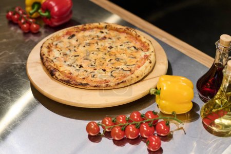 Foto de Pizza italiana caliente y apetitosa con champiñones sobre tabla redonda de madera rodeada de tomates rojos cereza frescos y pimienta amarilla - Imagen libre de derechos