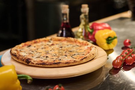 Téléchargez les photos : Focus sur une planche ronde en bois avec une pizza végétarienne appétissante et chaude entourée de tomates cerises fraîches mûres et de capsicums - en image libre de droit