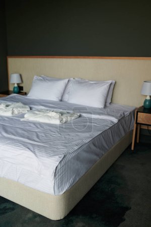 Téléchargez les photos : Fait partie du lit double confortable avec des draps et des oreillers bien rangés et deux peignoirs pliés blancs propres préparés pour les nouveaux clients de l'hôtel - en image libre de droit