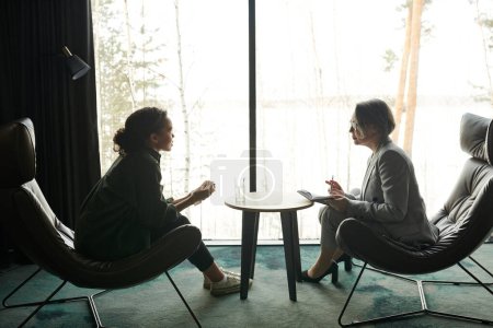 Photo for Young female patient and mature professional psychologist sitting in front of one another during discussion of problems and ways of solving them - Royalty Free Image